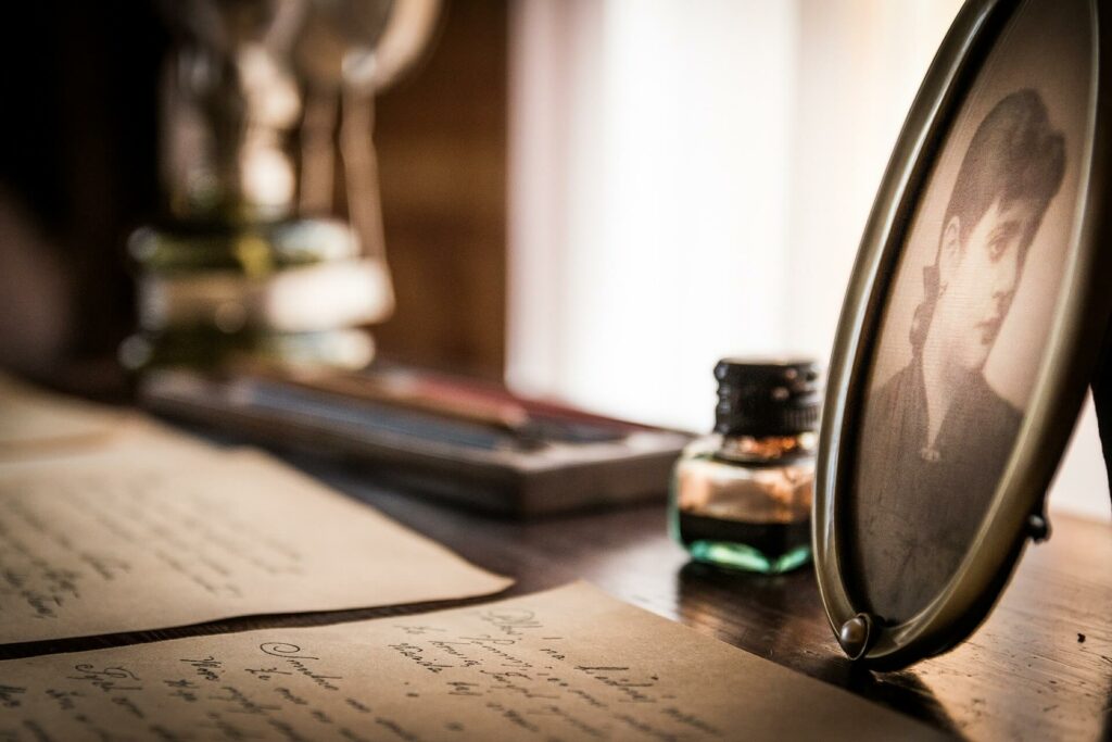 Handgeschriebene Briefe liegen auf einem Schreibtisch, daneben ein ovaler Bilderrahmen mit dem Bild einer Frau